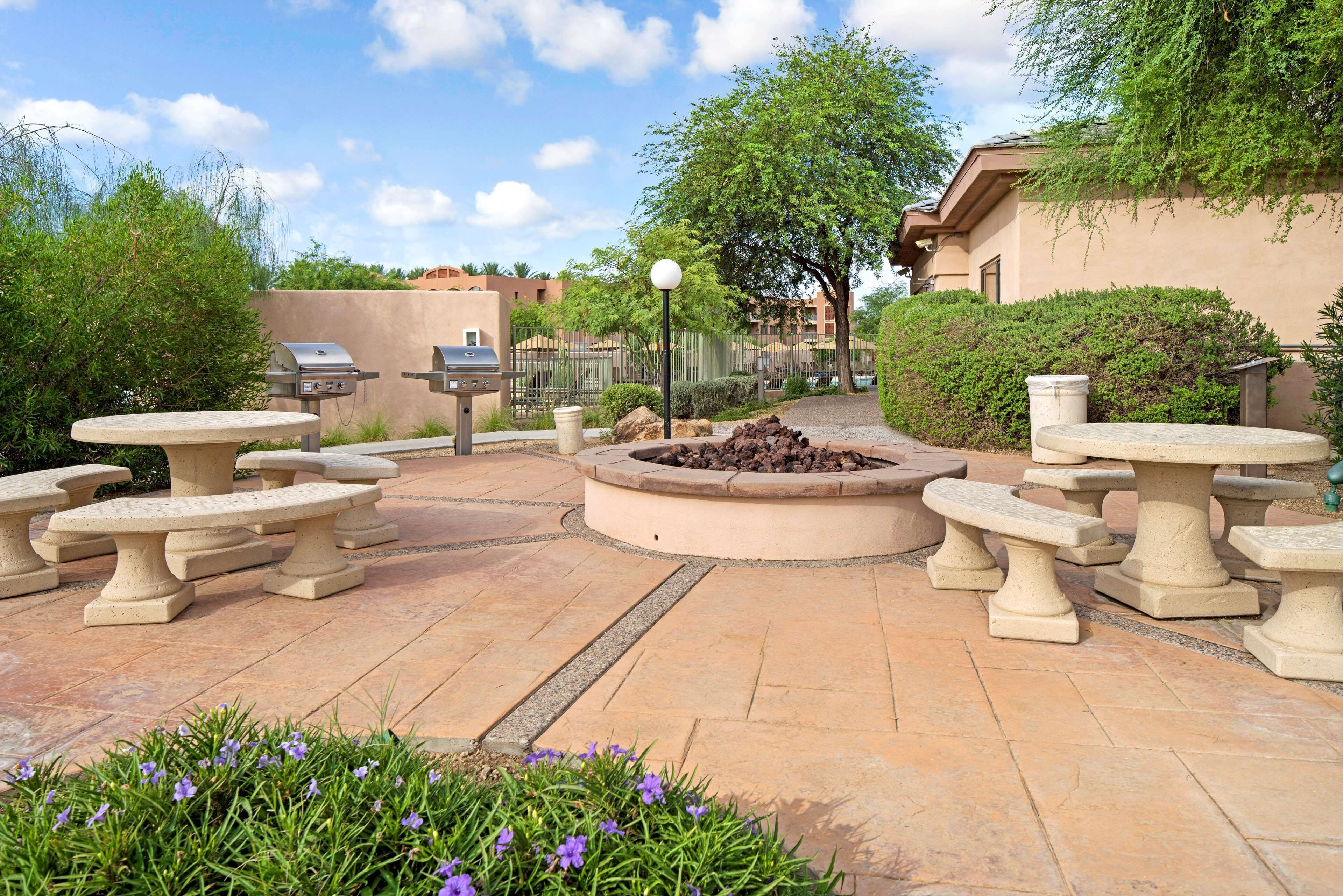 An outdoor patio with stone tables and benches, a fire pit, and a grill.