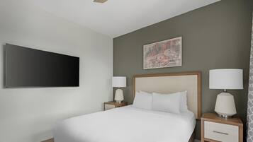 Habitación de hotel con una cama grande, dos mesitas de noche con lámparas, un televisor de pantalla plana y un elemento decorativo en la pared.