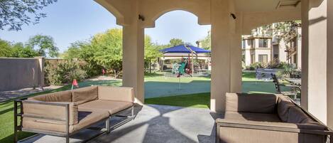 A covered outdoor seating area with two beige sofas, a concrete floor, and a view of a golf course and buildings in the background.