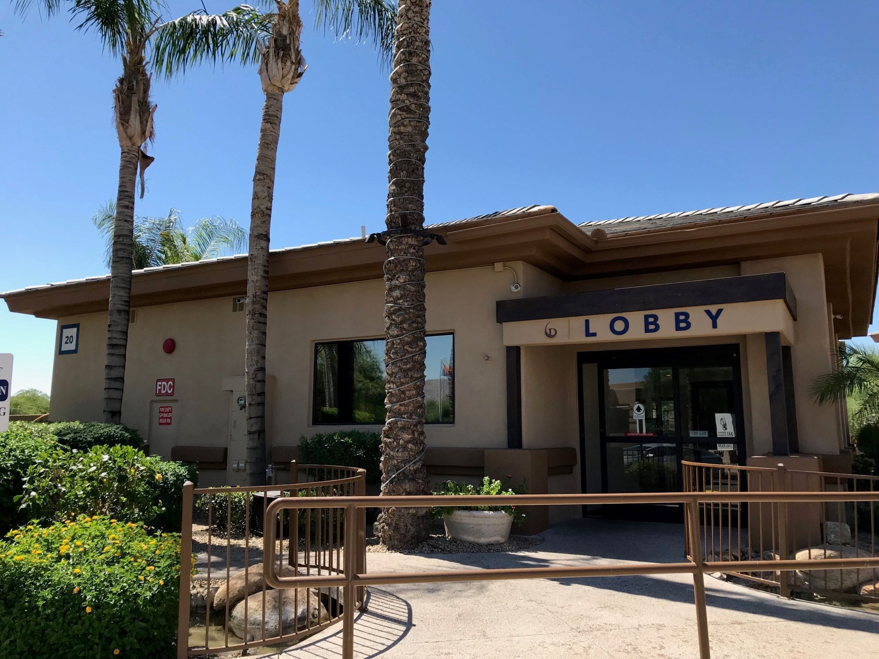A building with a sign reading "LOBBY" at the entrance, surrounded by palm trees and a gated entrance.