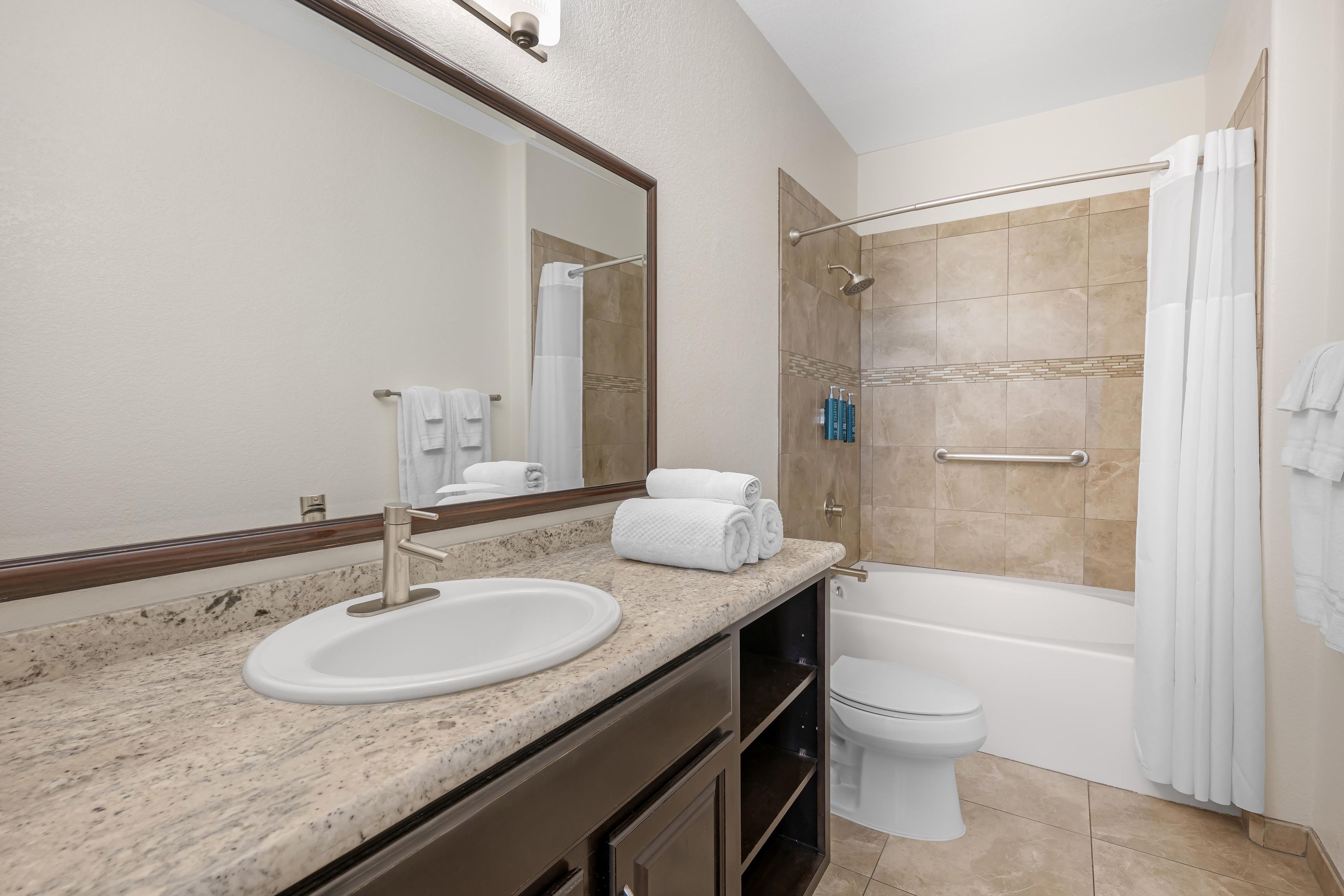A bathroom with a sink, mirror, toilet, and shower area.