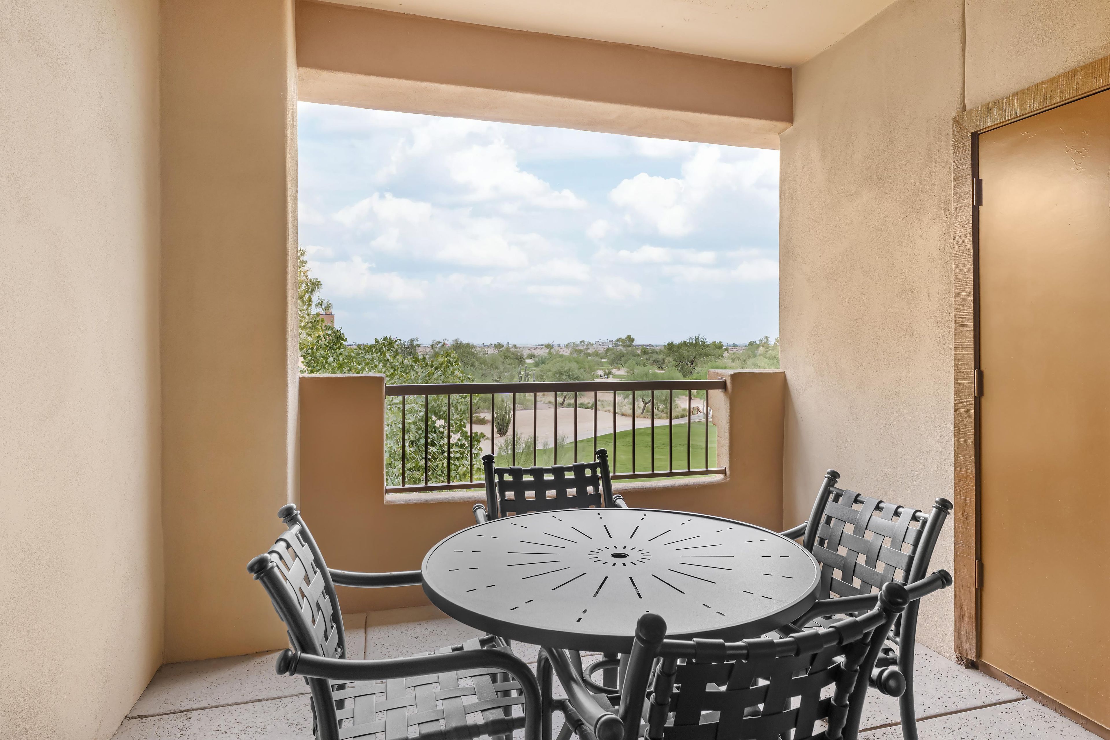 A balcony with a round table and four chairs, a view of a golf course, and a door to the right.