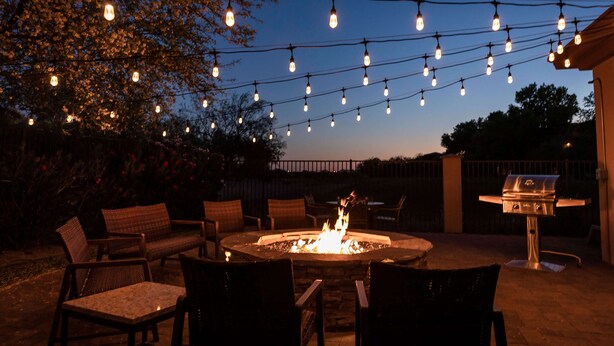 An outdoor patio with a fire pit, string lights, and outdoor furniture.