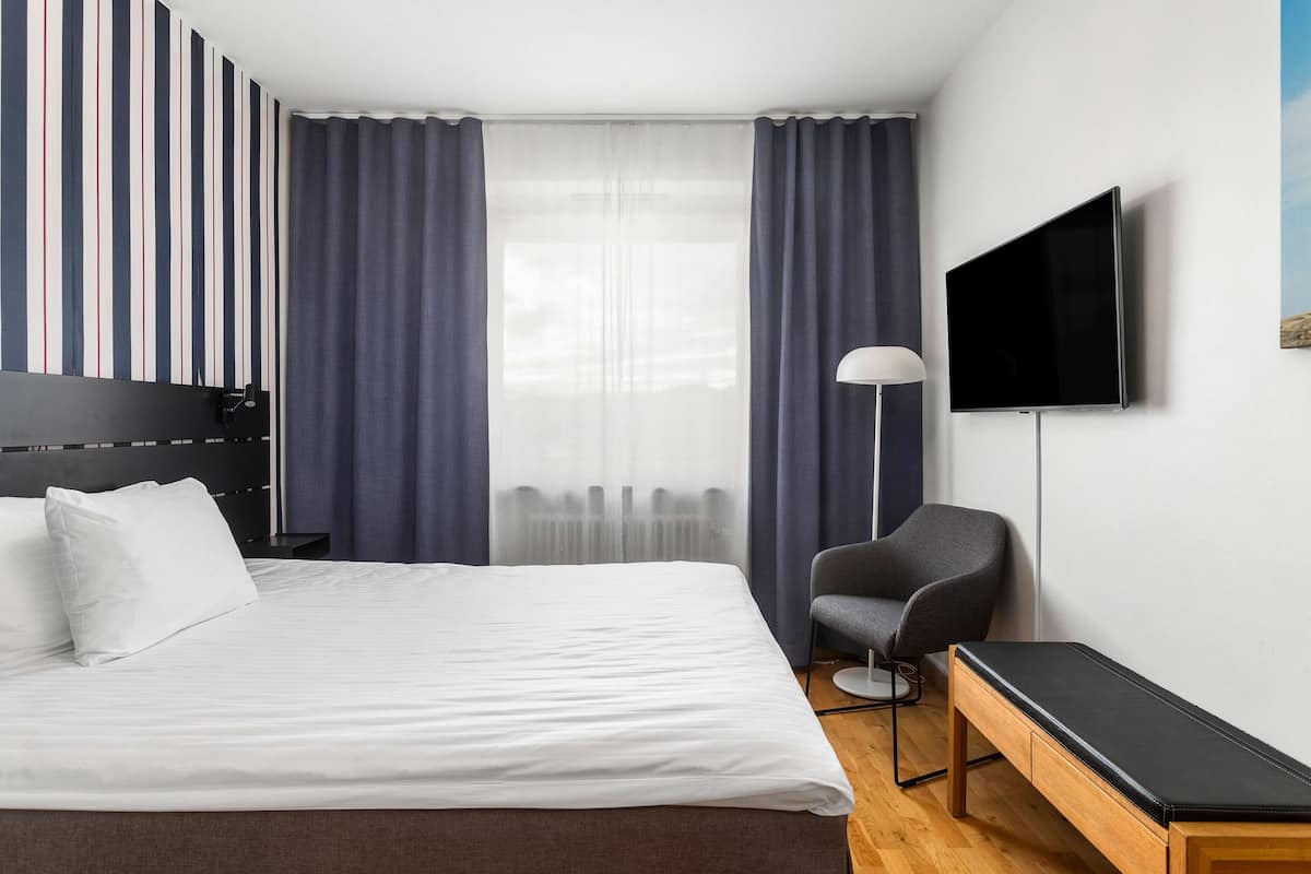 Una habitación de hotel moderna con una cama grande, un televisor montado en la pared, una silla y un banco.