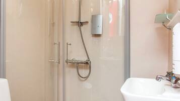Une salle de bain avec une douche à parois de verre, un lavabo blanc et un plancher en bois.