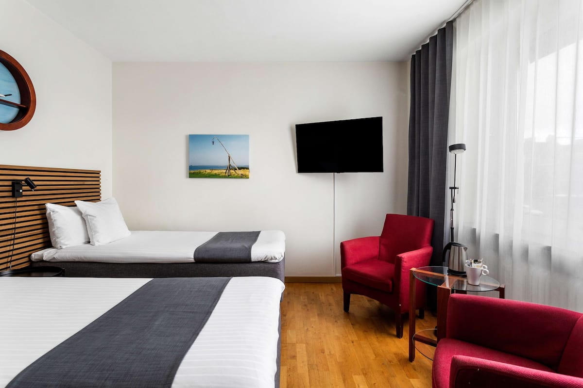 Una habitación de hotel con una cama, un sillón rojo, un televisor y un cuadro en la pared.