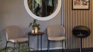 Ein modernes Interieur mit zwei Sesseln, einem kleinen Tisch mit Pflanze, einem runden Spiegel und einem schwarzen Kamin.