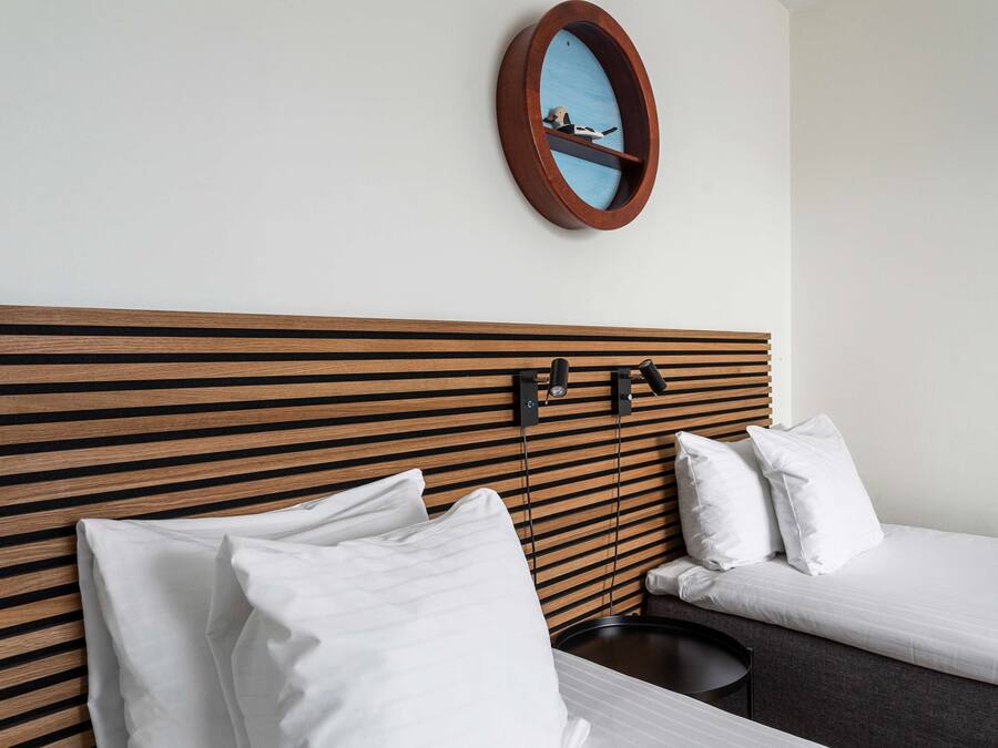 A hotel room with a wooden headboard, two white beds, a round mirror, and a small table.