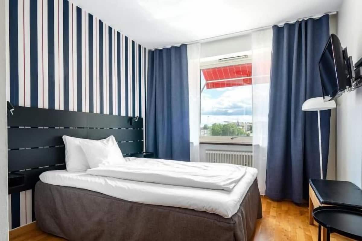 Una habitación de hotel con cama, escritorio, ventana con cortinas y pared a rayas.
