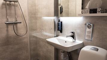 Un baño moderno con ducha envuelta en vidrio, un lavabo blanco y un inodoro.