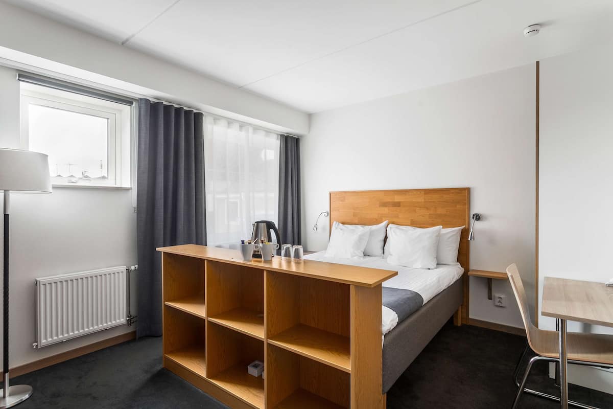 Una habitación de hotel con cama, una estantería de madera, un escritorio y una silla.