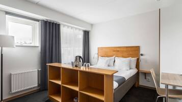 A hotel room with a bed, a wooden shelf unit, a desk, and a chair.