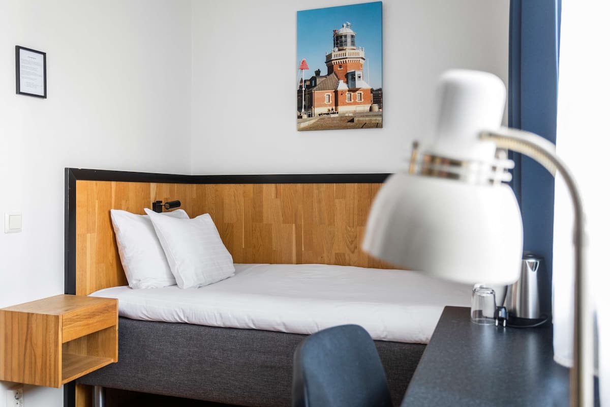 Una cama bien hecha con ropa blanca, un cabecero de madera y una mesita de noche de madera con una lámpara.