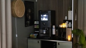 Ein gemütlicher Wohnraum mit Kaffeemaschine, Fernseher und einem kleinen Regal mit Tassen und Kerze.