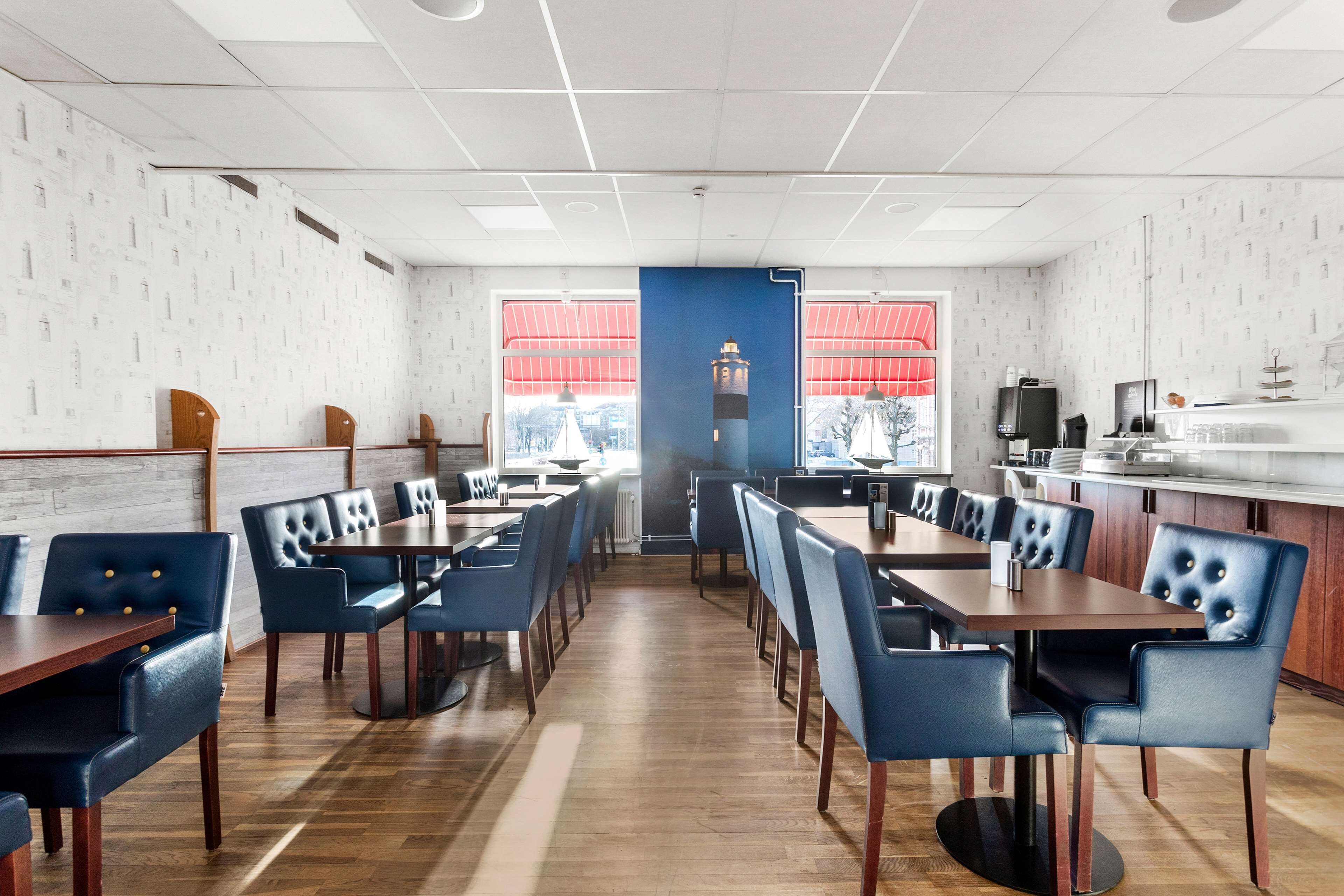 Un restaurant doté d’un plancher en bois, de chaises recouvertes d’un tissu bleu et offrant une vue sur un phare à travers de grandes fenêtres.