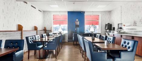 A restaurant with wooden flooring, blue upholstered chairs, and a view of a lighthouse through large windows.