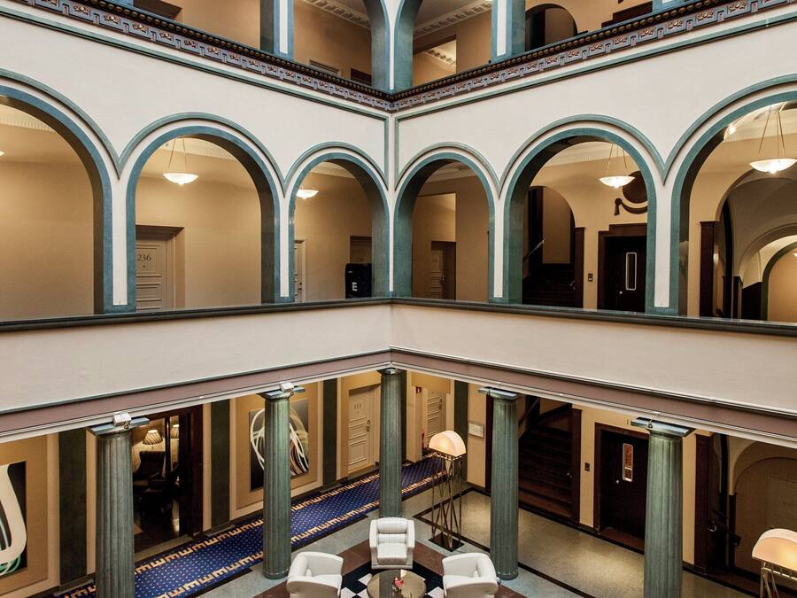 A multi-level atrium with a checkered floor, seating areas, and a central column with a vase.