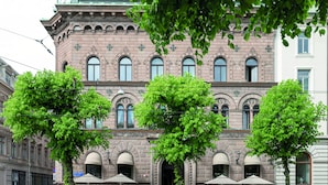 Ein historisches Gebäude mit einem zentralen Eingang, großen Fenstern und Außenbereichen mit Sitzgelegenheiten.