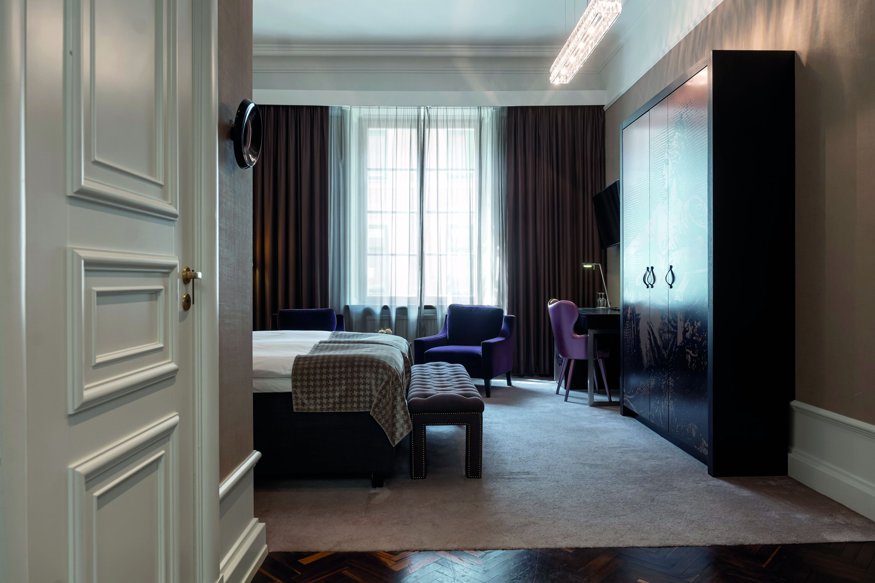 Una habitación de hotel con cama, escritorio, silla y un armario grande.
