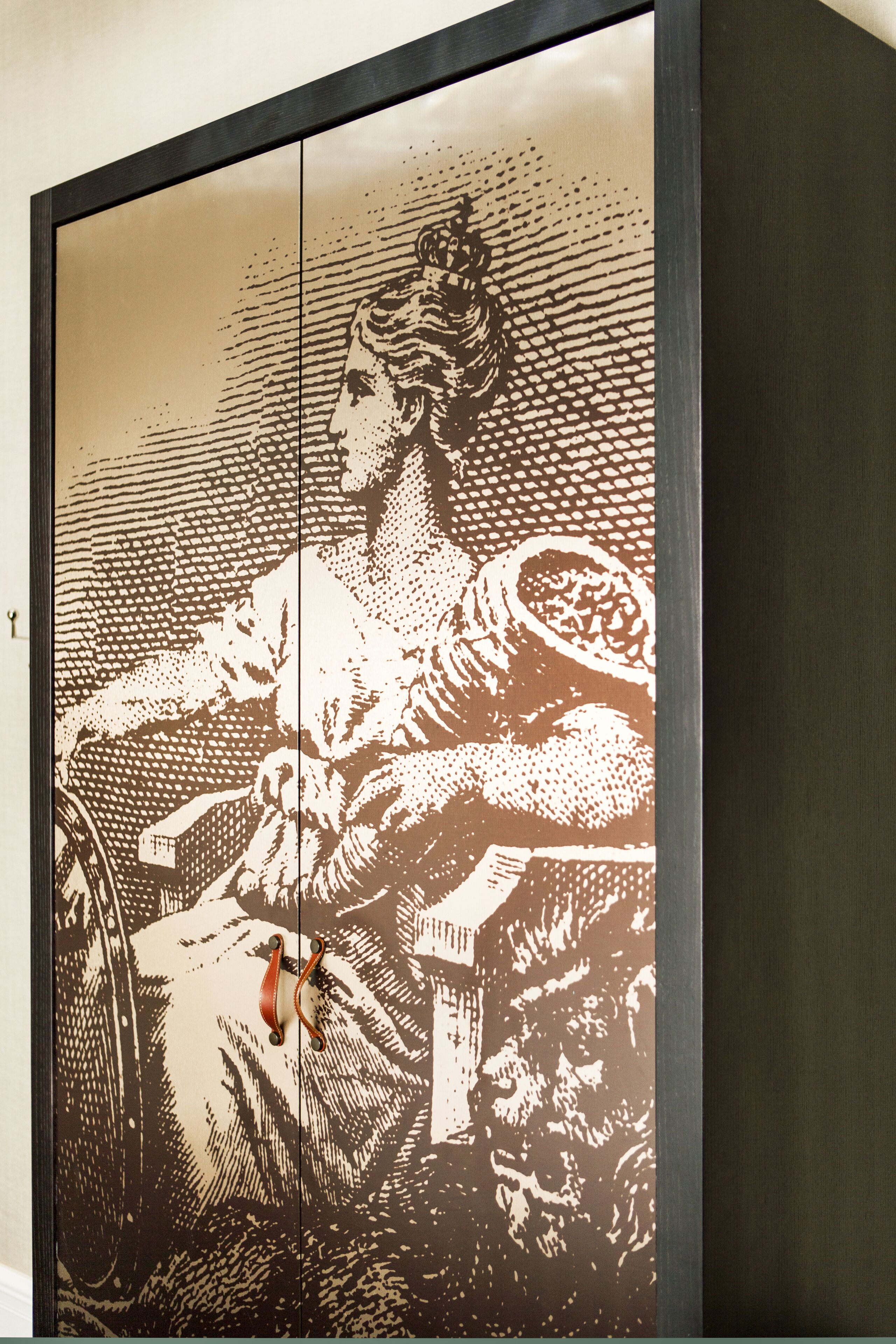 A framed artwork depicting a person in traditional attire, possibly a historical figure, seated with a bowl and a small table.