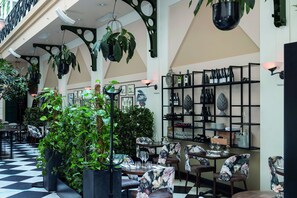 Un restaurante con suelo a cuadros, plantas colgantes, sillas con motivos florales y botellas de vino en estanterías.