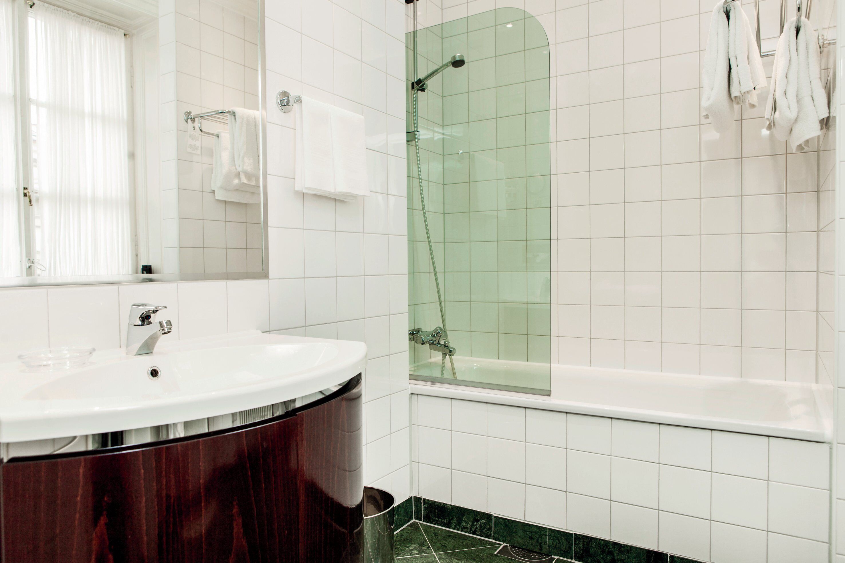 Un baño con lavamanos blanco, espejo, ducha con cerramiento de vidrio y bañera.