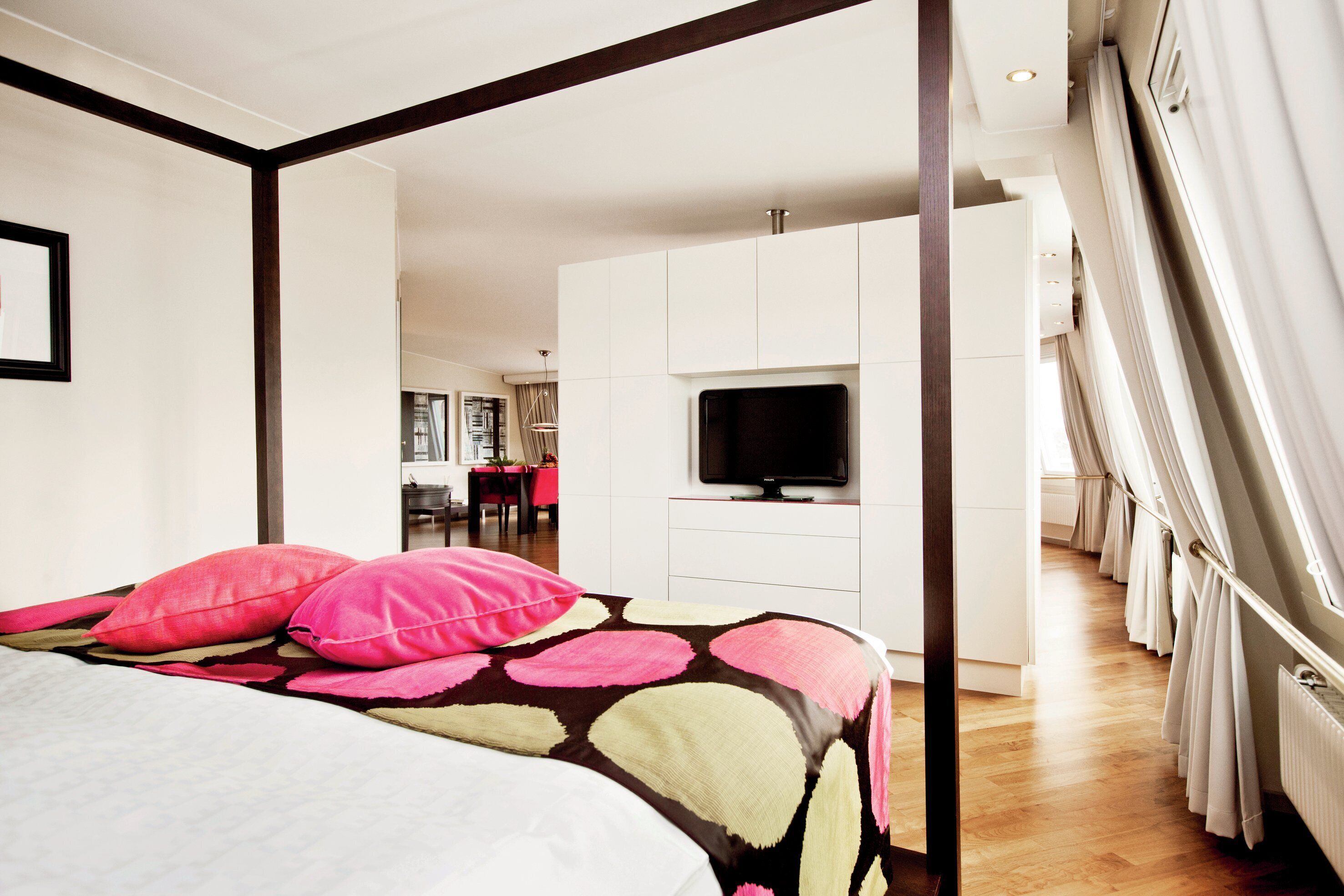 A bedroom with a bed, a television, and a view of a dining area.