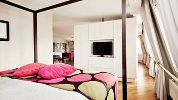 A bedroom with a bed, a television, and a view of a dining area.