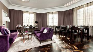 A spacious living room with a herringbone wood floor, purple armchairs, a coffee table, and a dining area with a chandelier.