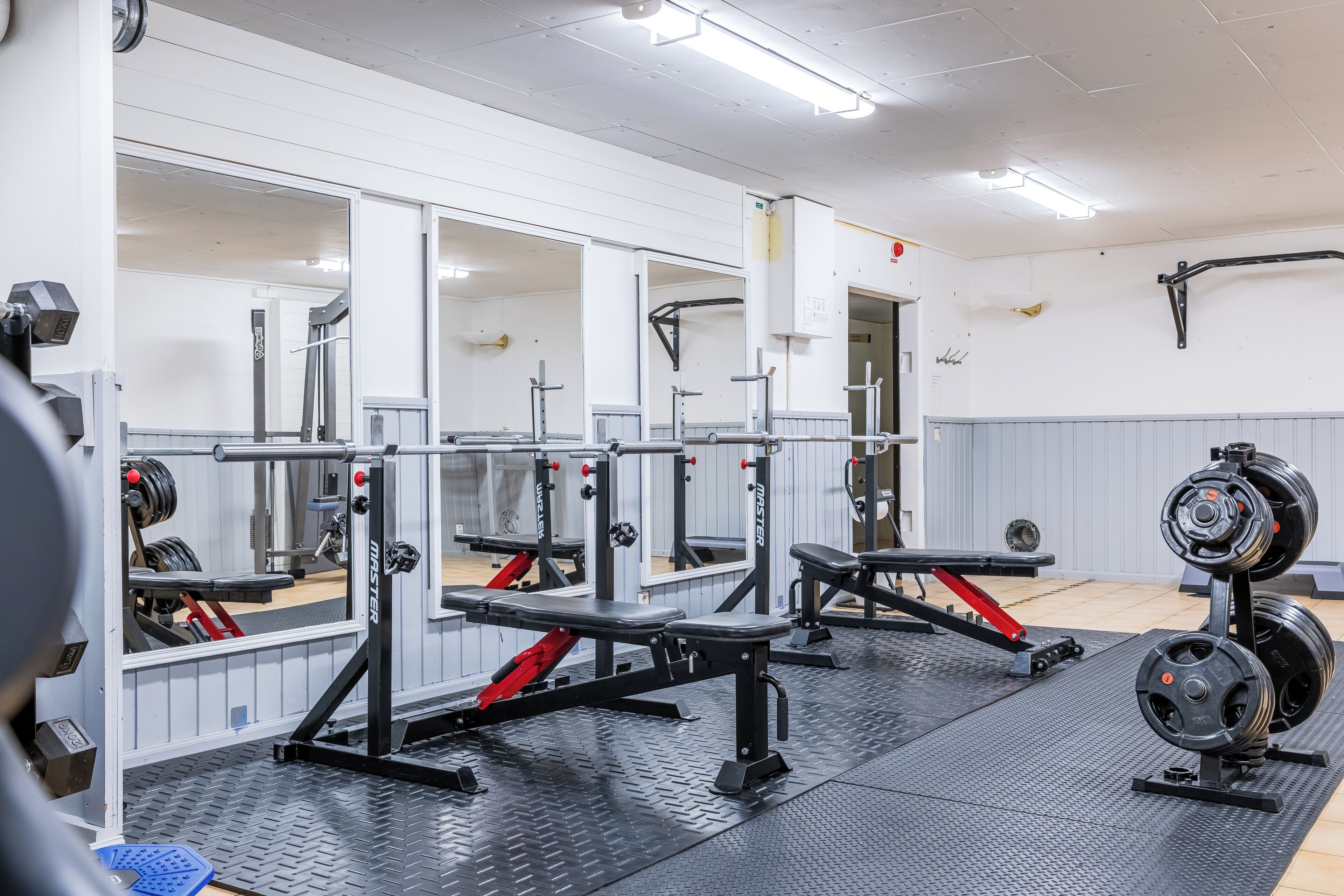 Ett gym med utrustning för styrketräning, speglar och ett svart gummigolv.