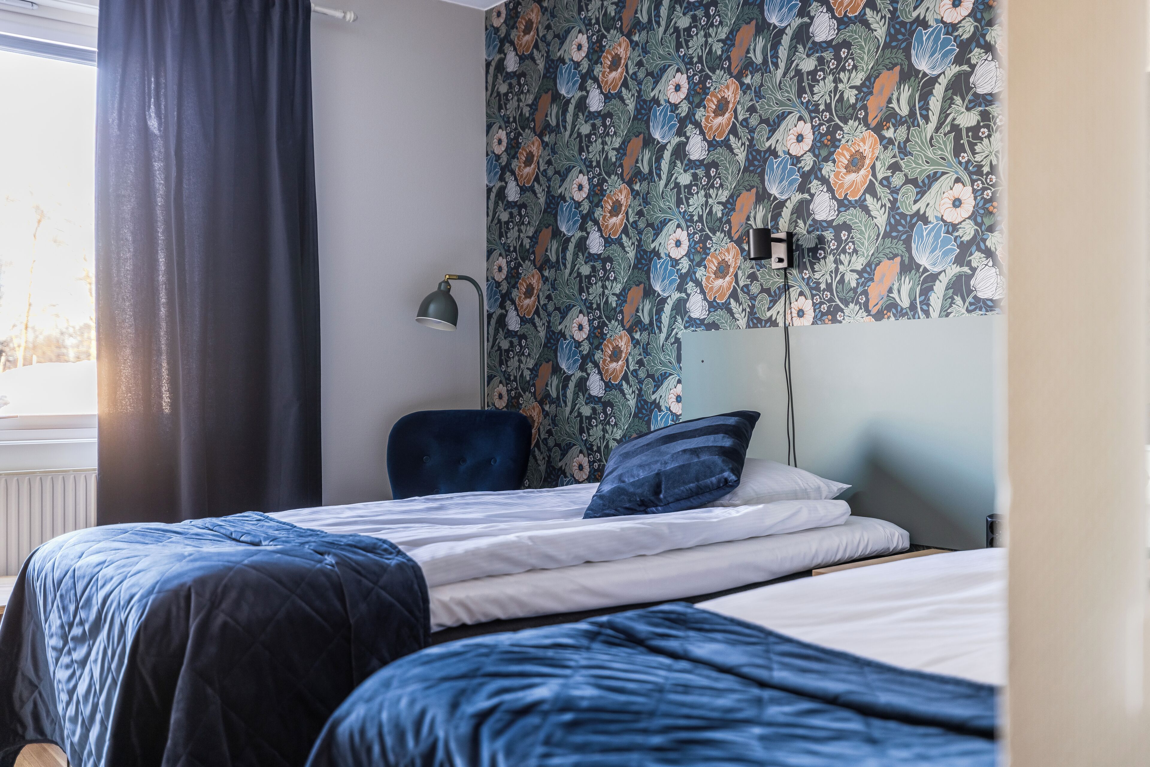 A bedroom with a bed, a chair, and a wall with floral wallpaper.