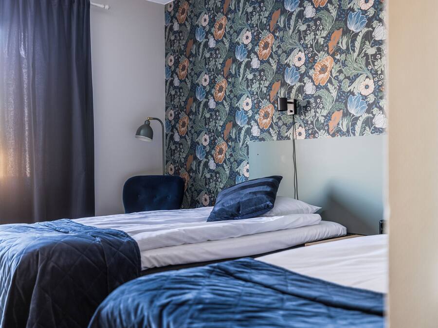 A bedroom with a bed, a chair, and a wall with floral wallpaper.