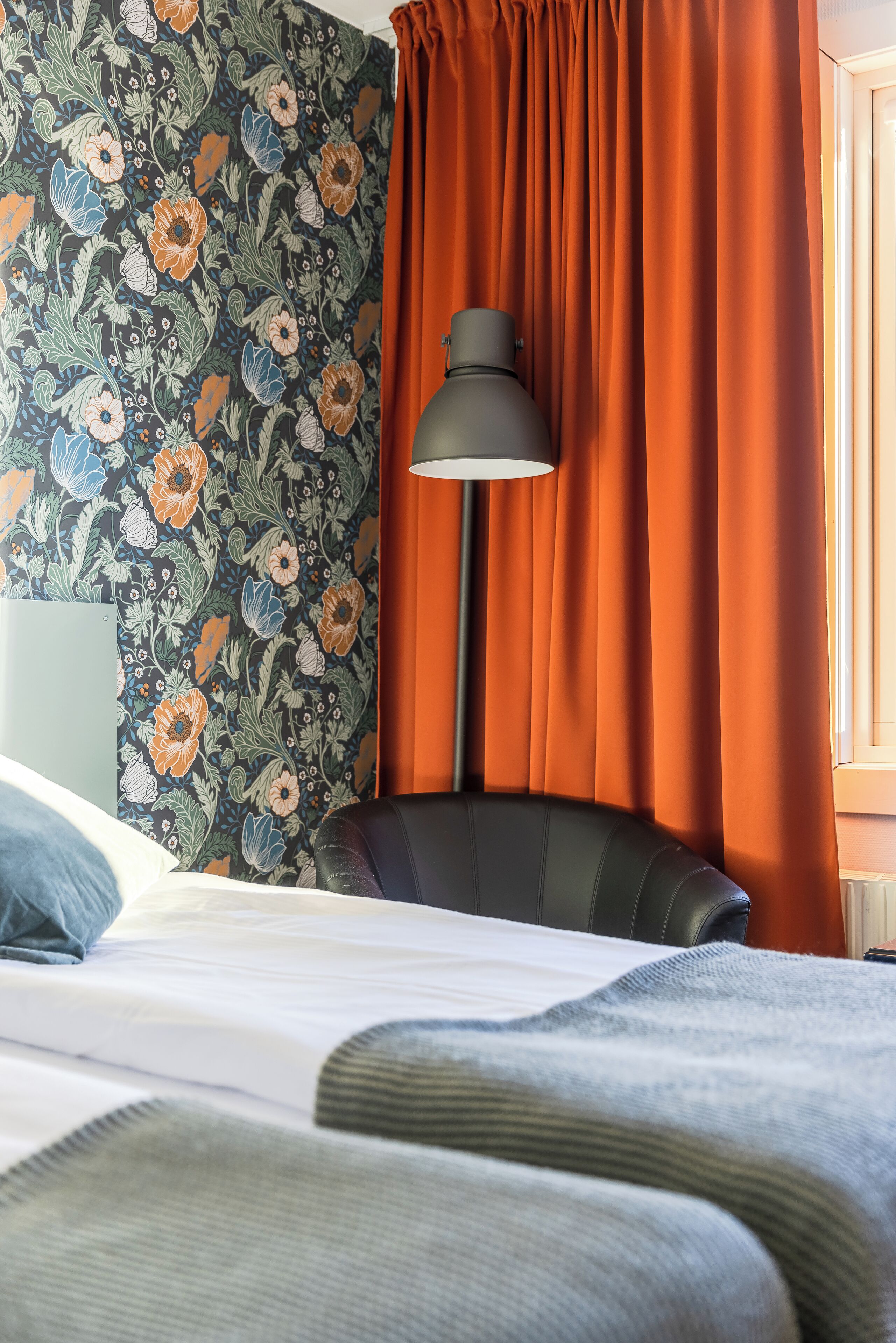 A hotel room with a bed, a chair, a lamp, and a window with curtains.