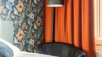 A hotel room with a bed, a chair, a lamp, and a window with curtains.