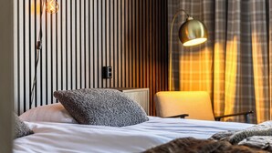 Una cama bien tendida con una almohada, una lámpara de noche y una pared con líneas verticales.