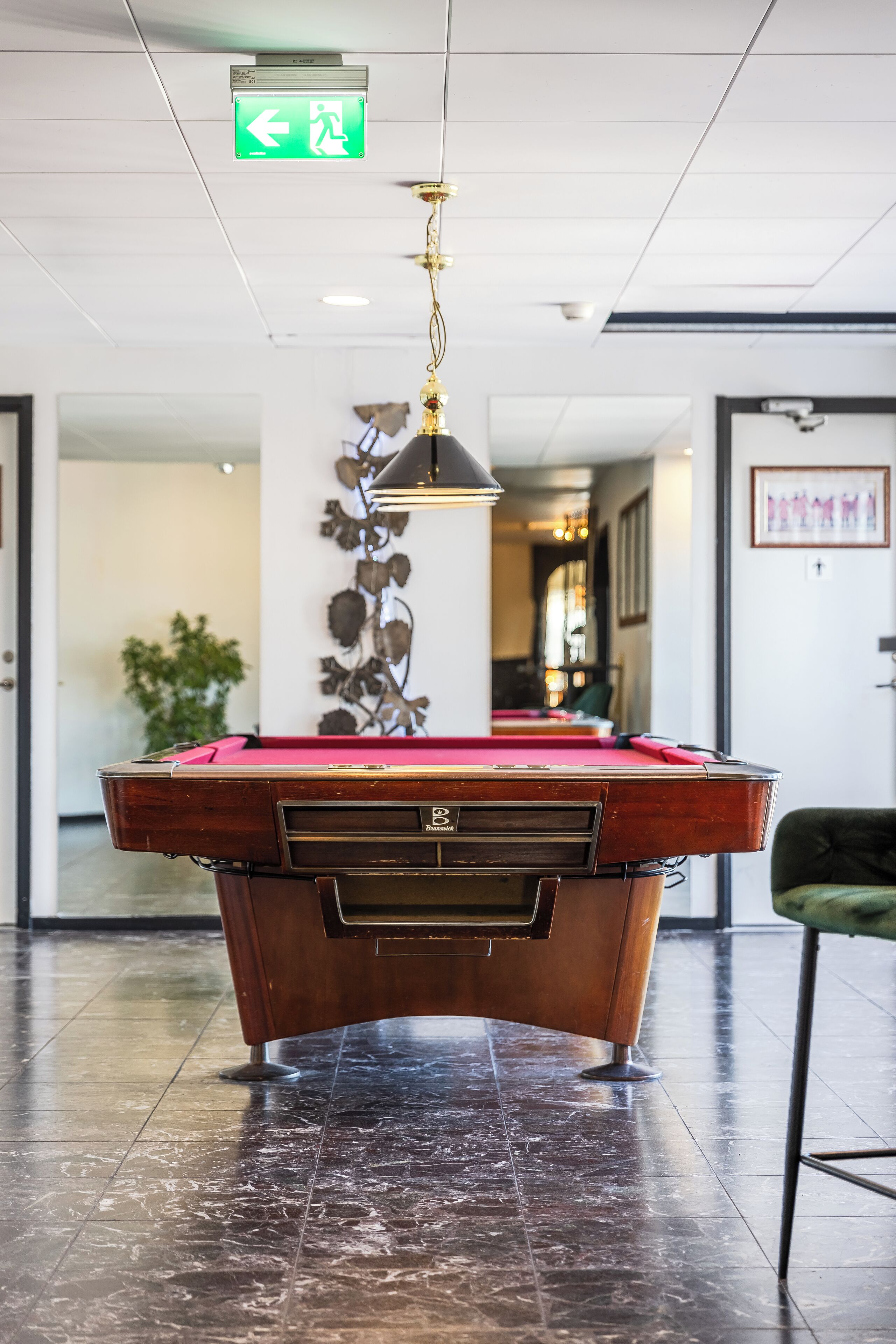 A pool table in a lobby with a green exit sign above it.
