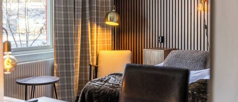 A hotel room with a bed, a chair, a small table, a lamp, and a window with curtains.