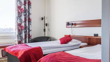 Habitación de hotel con dos camas, un escritorio, una silla, un radiador y una ventana con cortinas.