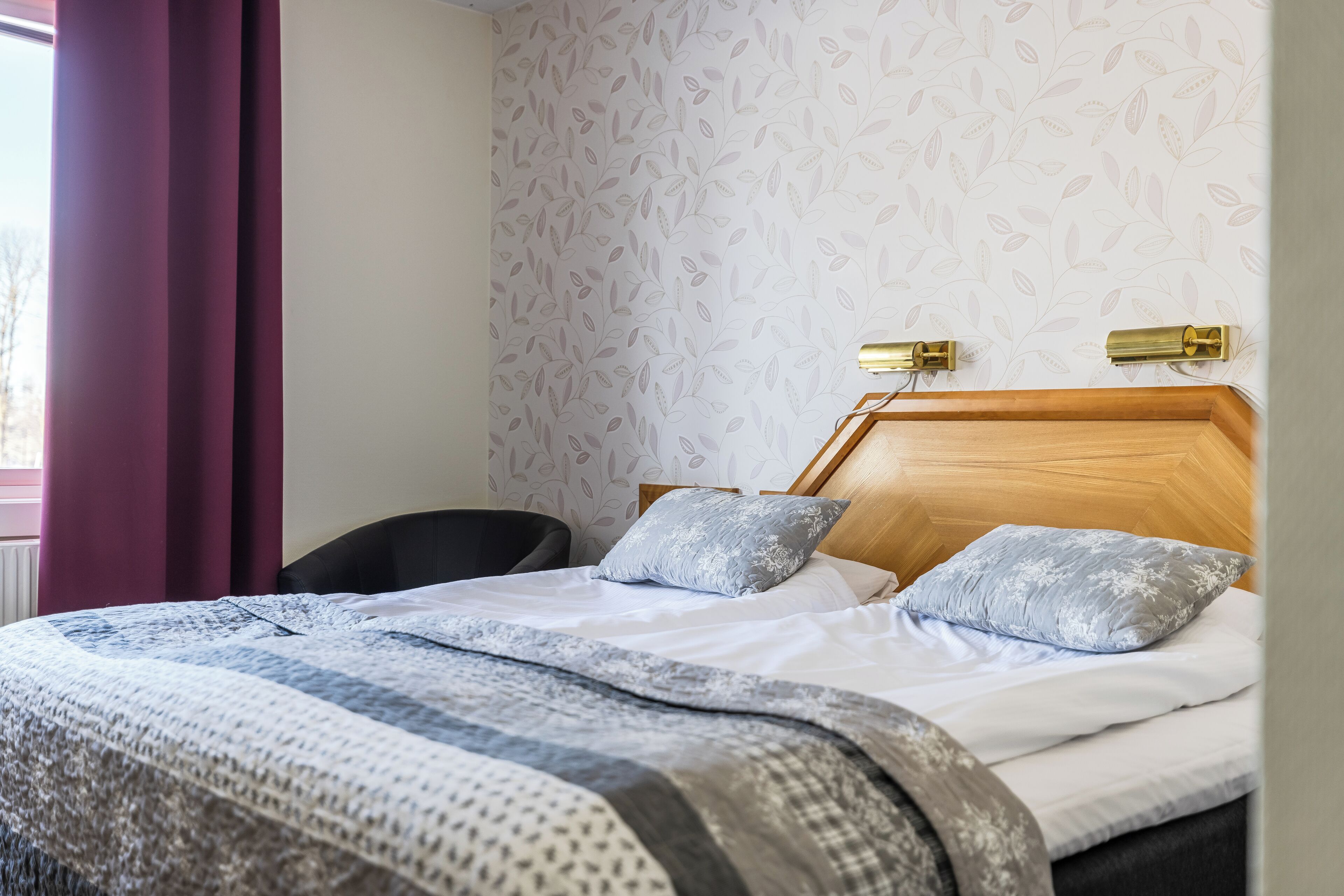 A neatly made bed with patterned bedding, a wooden headboard, and two wall-mounted lamps.