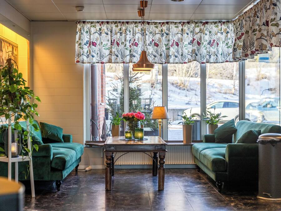 Un salon chaleureux avec un canapé vert, une table en bois ornée d’un vase de fleurs et une vue sur un paysage enneigé, visible à travers de grandes fenêtres.