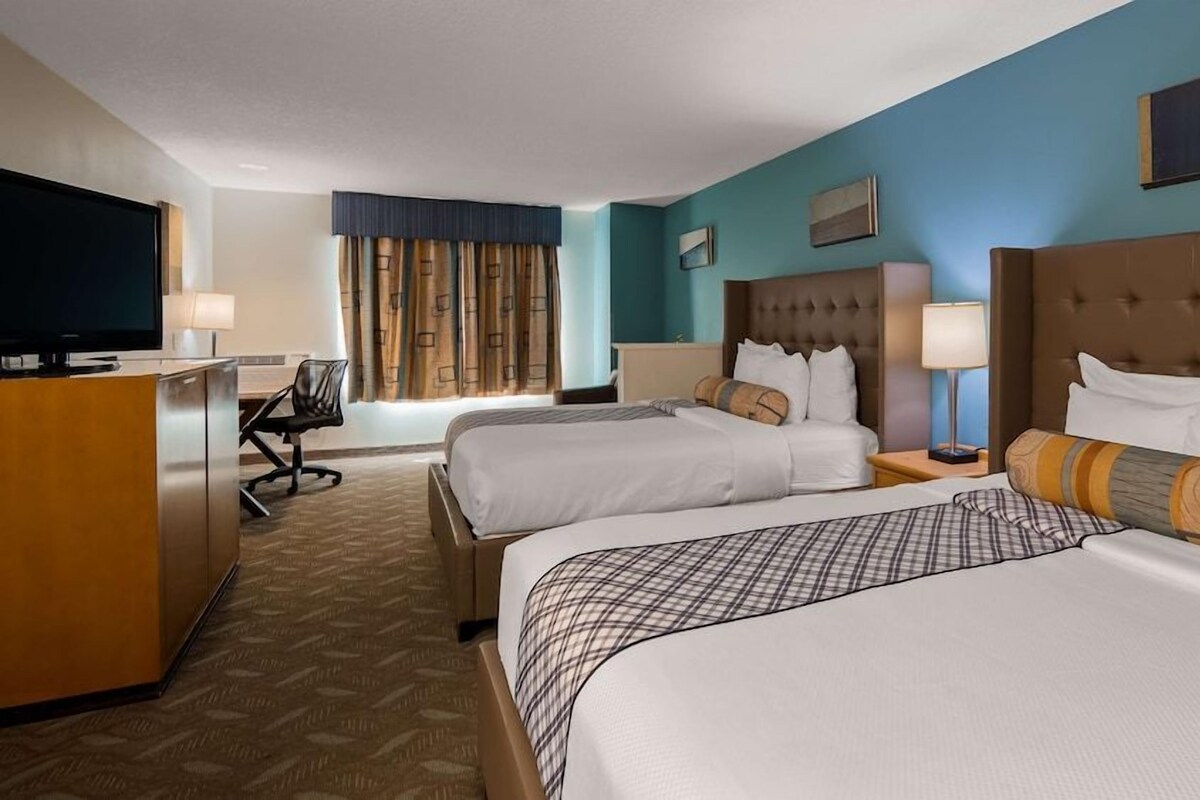 A hotel room with two beds, a desk, a television, and a window with curtains.