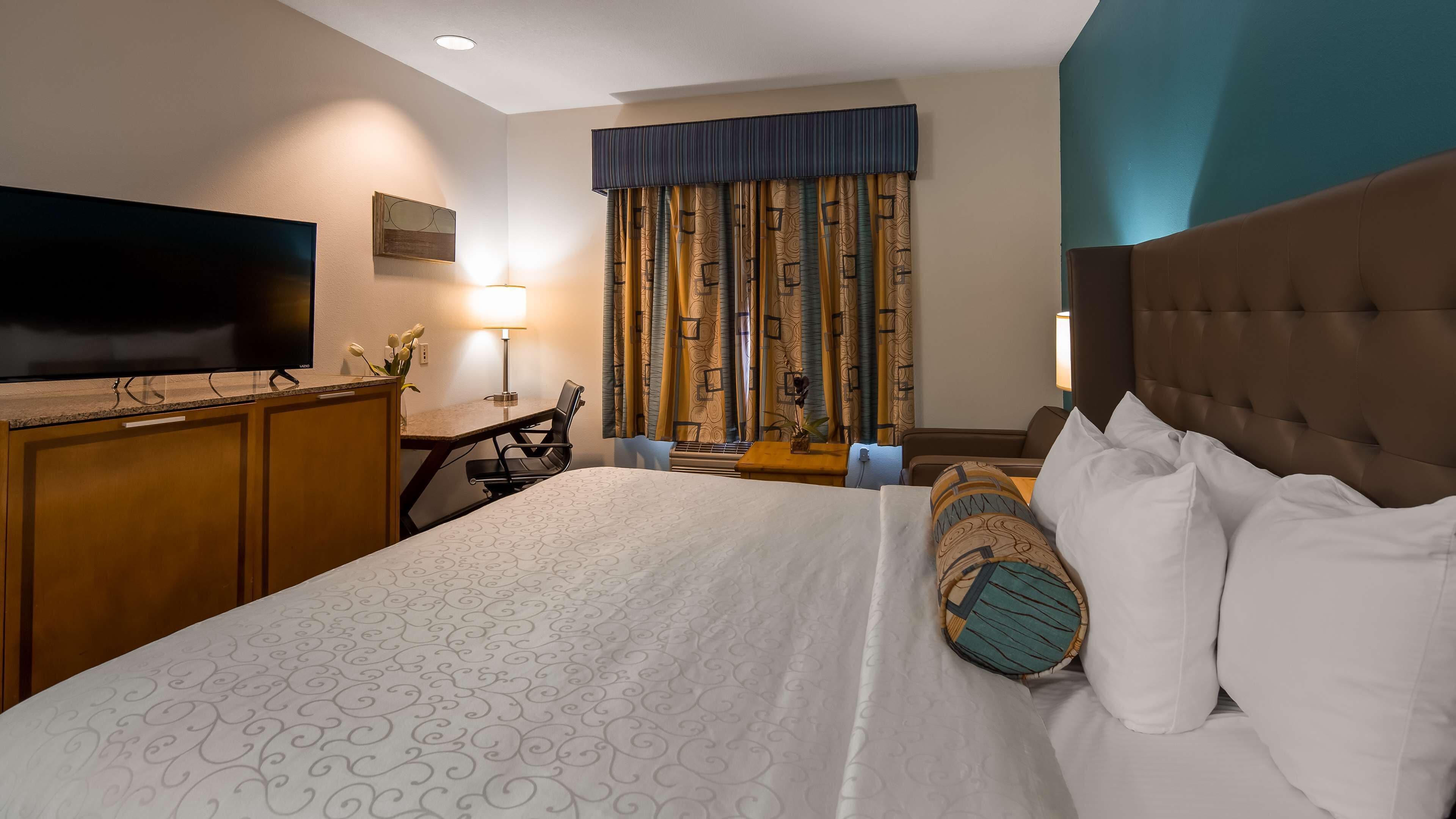 A hotel room with a large bed, a television, a desk with a chair, and a window with curtains.