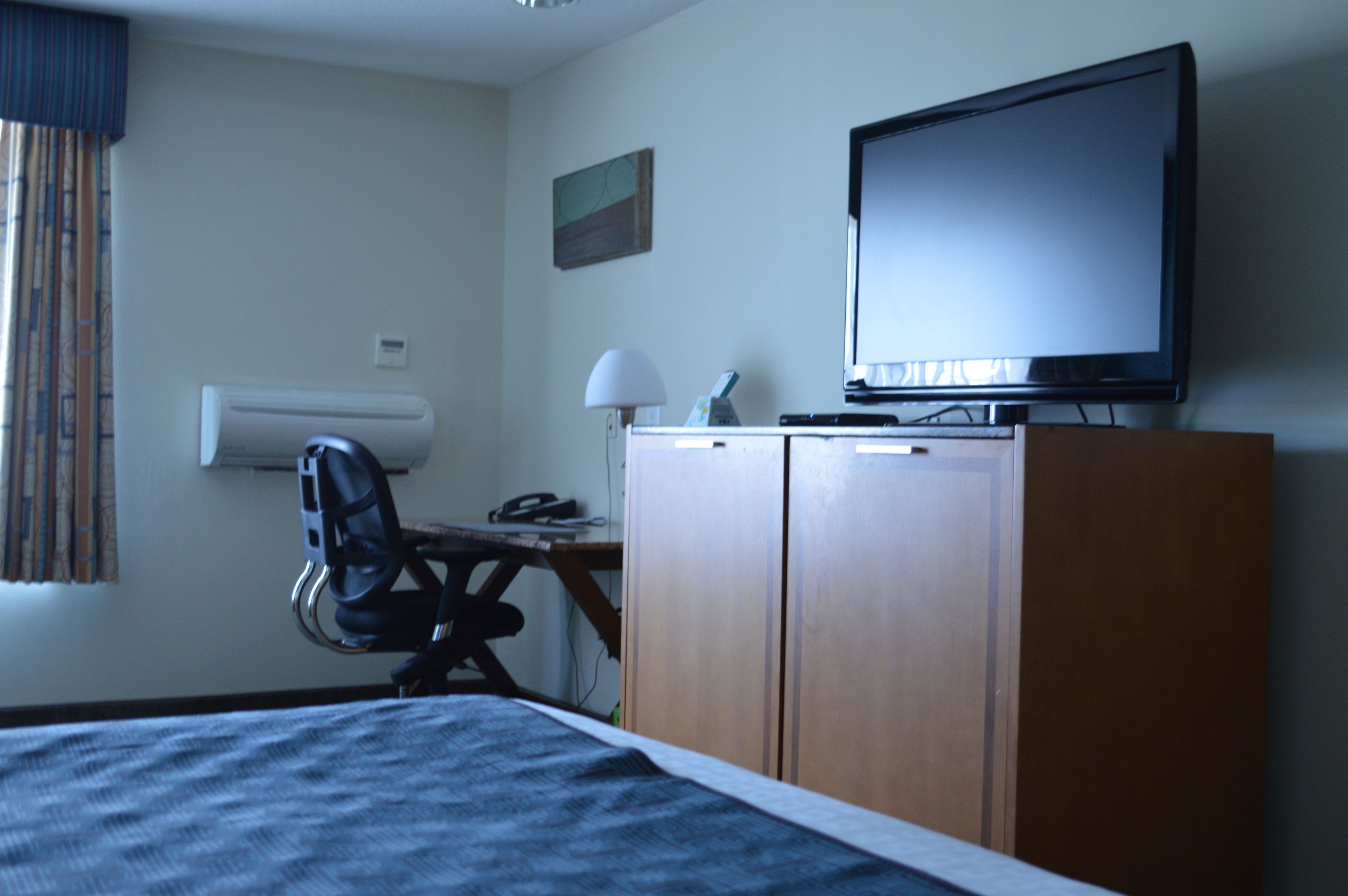 Una camera d'albergo con un letto, una scrivania con una sedia, una televisione e un armadio.