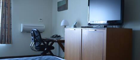 Una camera d'albergo con un letto, una scrivania con una sedia, una televisione e un armadio.