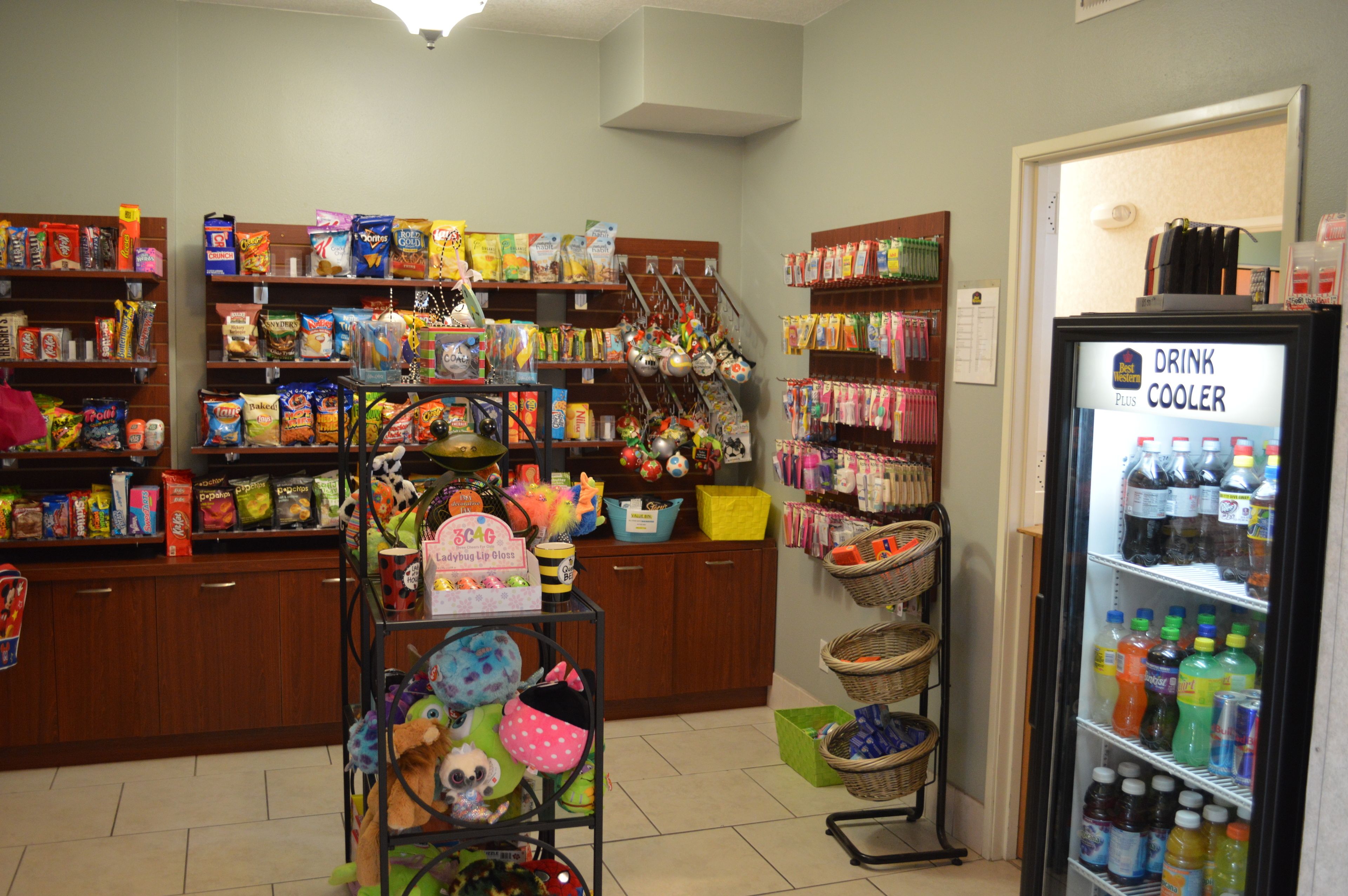 A store with shelves stocked with snacks, a drink cooler, and baskets.