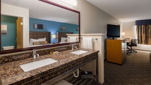 A hotel bathroom with a granite countertop, two sinks, a large mirror, a television, and a bed with a headboard. - Best Western Plus Liberty Lake Inn (Liberty Lake)