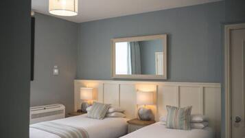 A hotel room with two beds, a large mirror above the beds, and bedside lamps.
