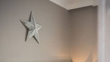 A neatly made bed with white linens and a checkered pillow, a bedside lamp, and a star decoration on the wall.