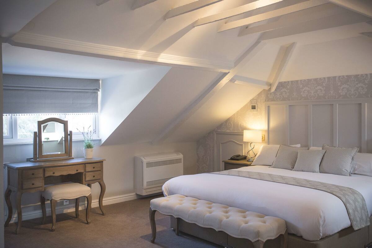 Une chambre avec un grand lit, une coiffeuse avec un miroir et une fenêtre avec des stores.