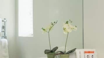 A bathroom with a white sink, two orchid plants in green pots, a star decoration on the wall, and a towel rack.